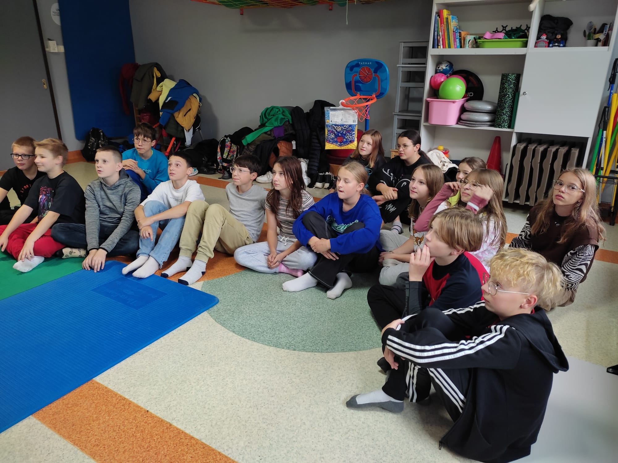 Uczniowie siedzą na dywanie, w tle sprzęt do rehabilitacji 